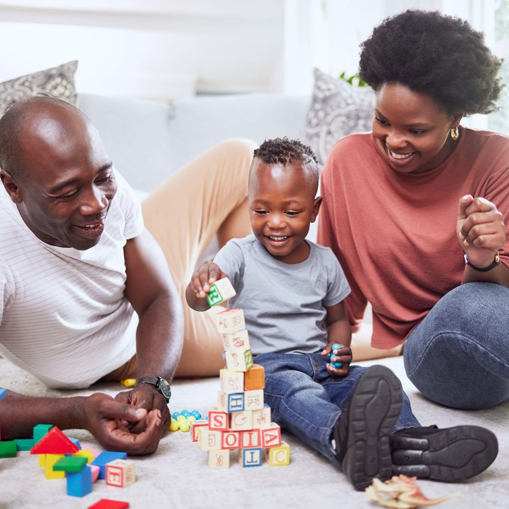 Young family sitting on the carpet playing with letter blocks with their young son